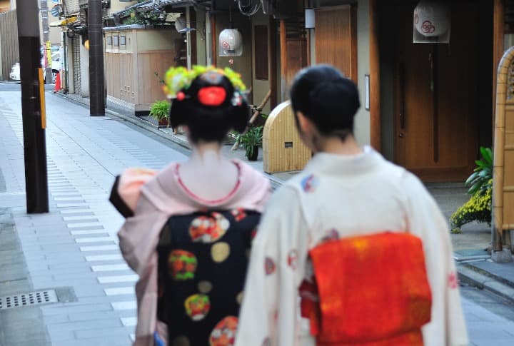 dos chicas vestidas de forma tradiconal japonesa, de espaldas, caminando por el barrio de gion, en kioto - weroad