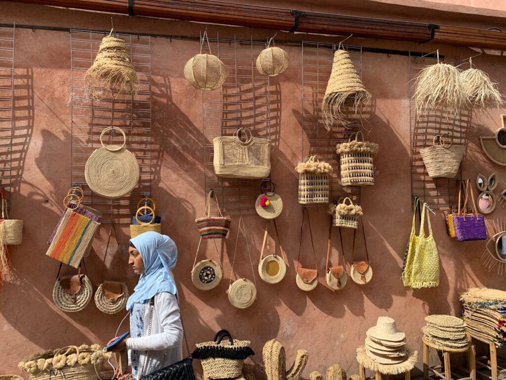 mujer paseando en la medina, algo que ver en marrakech, bolsos y objetos de paja colgados a una pared del mercado