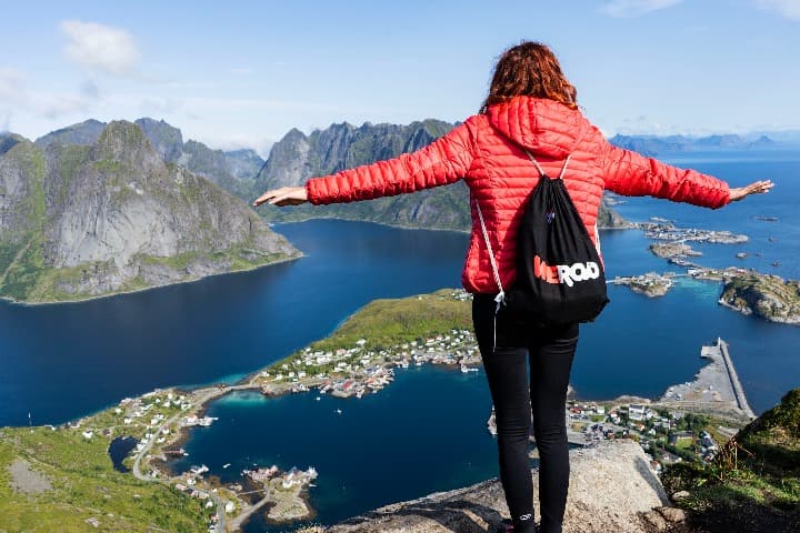 chica de espaldas y con brazos abiertos con mochila de weroad mirando desde un promontorio los fiordos en lofoten