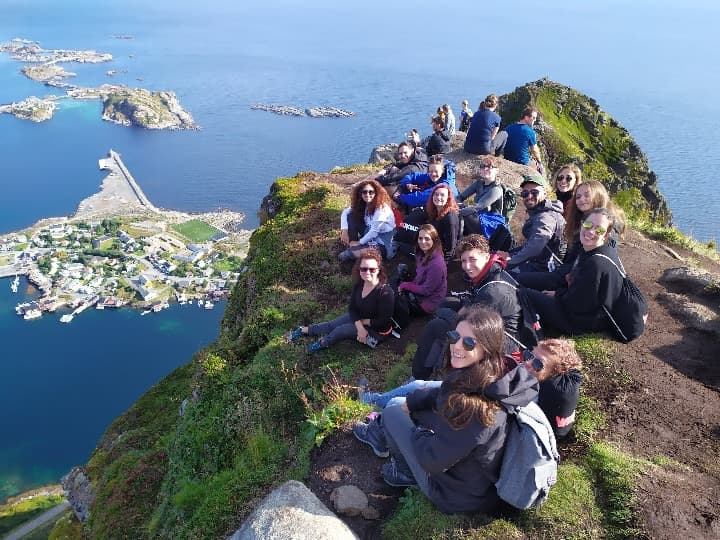 grupo de viajeros weroad sentados en la cima de una montaña, abajo panorama de lofoten y fiordos, algo que ver en noruega