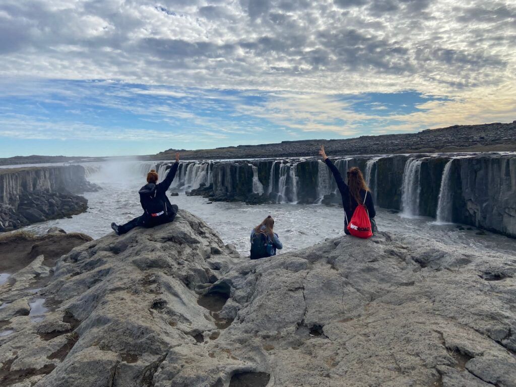Tres personas sentadas en unas rocas en Islandia mirando una cascada
