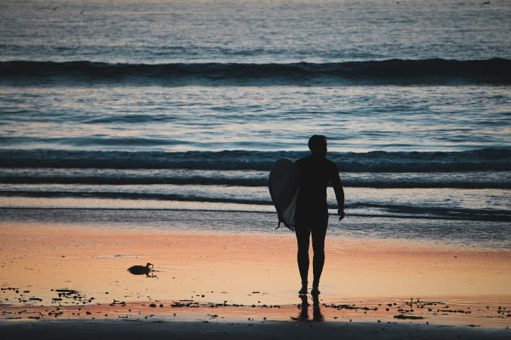 surfero con tabla bajo el brazo caminando hacia el mar en mission beach, algo que ver en san diego - weroad