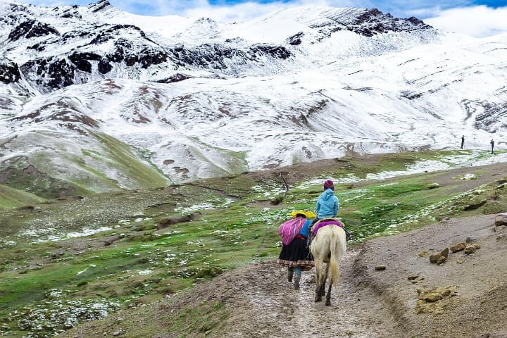 personas paseando por un sendero vistas de espaldas, una encima de un caballo, caminan hacia una montaña con nieve - weroad