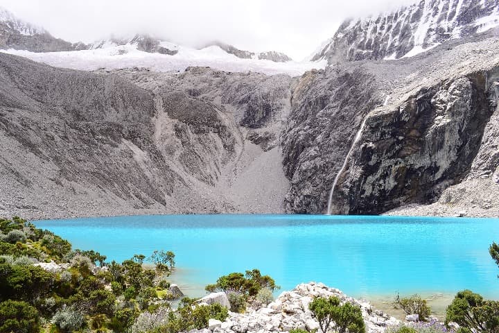 lago de huaraz en perú, agua azul y montañas detrás - weroad