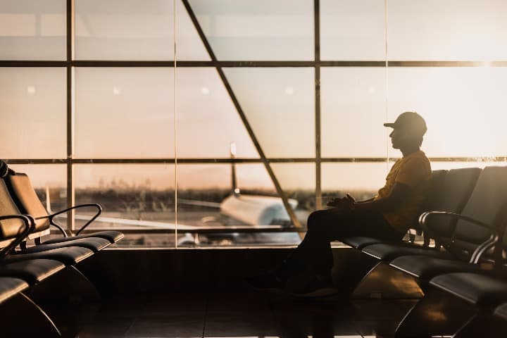 chico con gorro sentado en un aeropuerto, ventanal al fondo con avion en pista - weroad