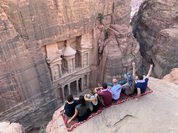viajeros weroad de espaldas sentados en una roca y mirando la puerta del tesoro de petra - weroad
