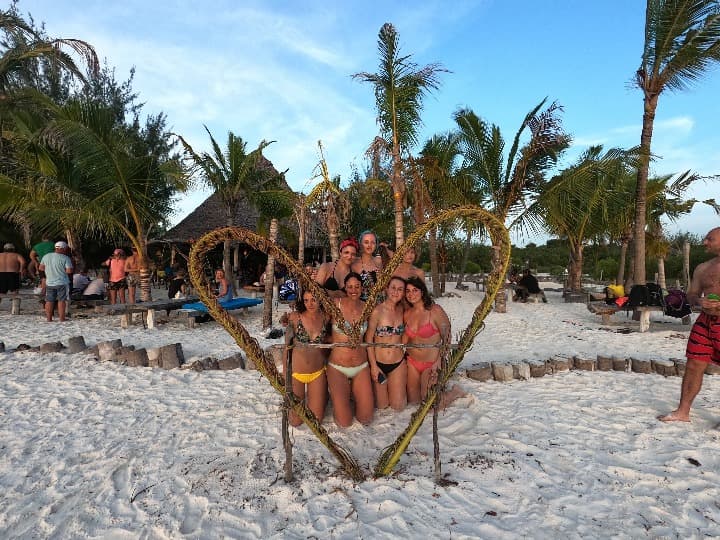 grupo de viajeros weroad en una playa posando detrás de un corazón hecho con arbustos en zanzibar
