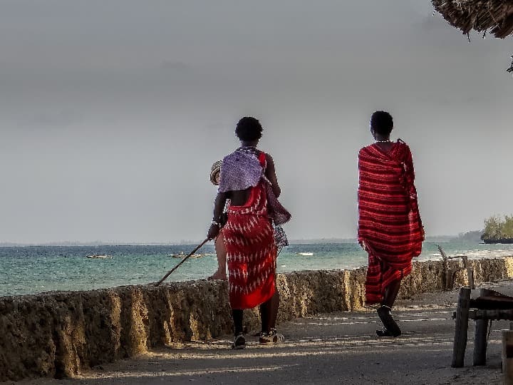 ds personas en vestidos típicos de zanzibar caminan de espaldas cerca del mar, en uroa - weroad