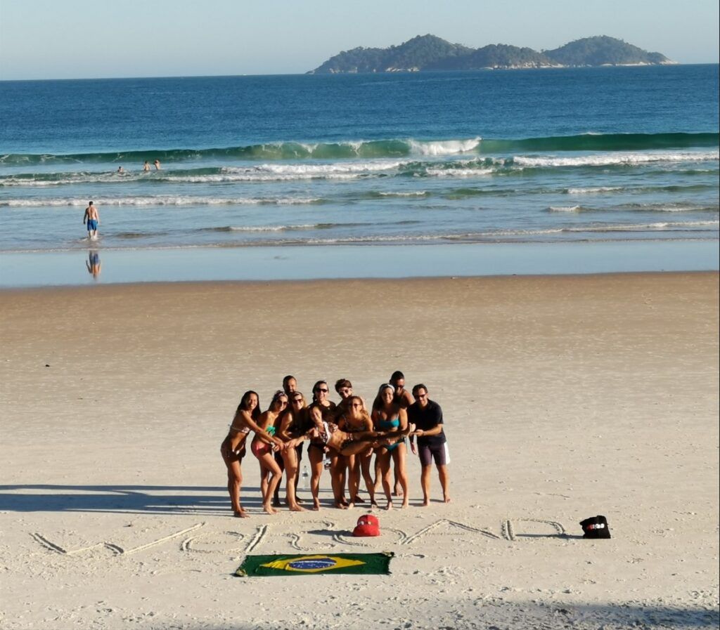 grupo de viajeros weroad en una playa de brasil, detrás el mar, delante na bandera del país 