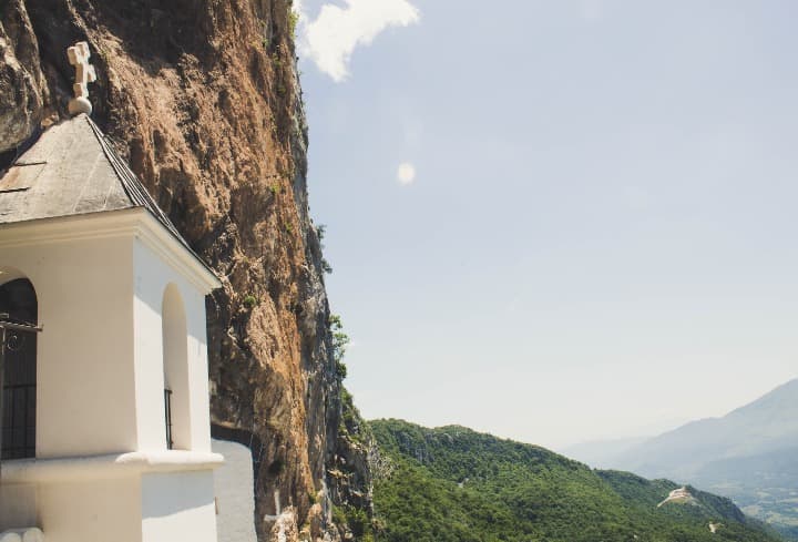 campanario blanco del monasterio de ostrog en montenegro, detrás verde de las montañas - weroad
