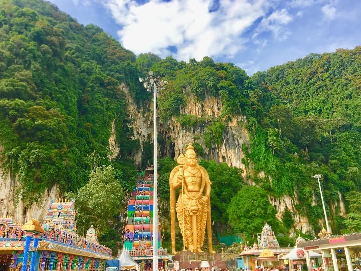 enorme estatua dorada con detrás acantilado con vegetacion y escaleras de colores en cuevas de Batu, malasia - weroad