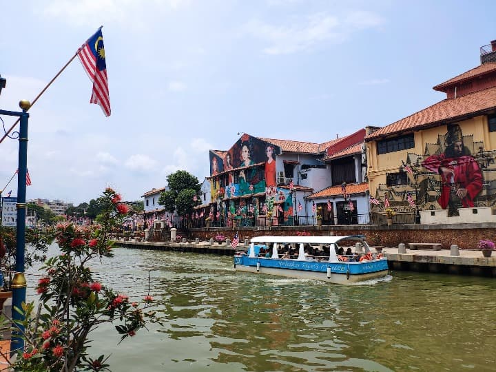 barco navegando rio con casas y bandera en primer plano, Melaka, malasia - weroad