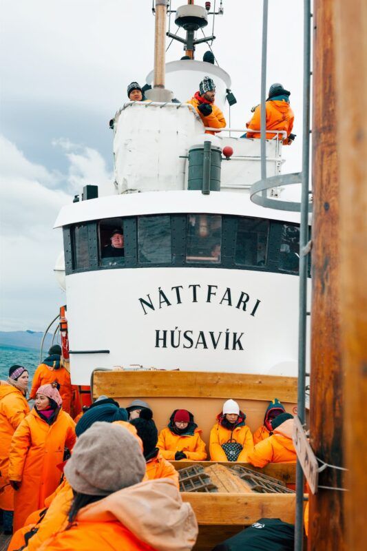 barco para excursión de avistamento de ballenas en husavik, islandia, pesonas con mono naranja - weroad