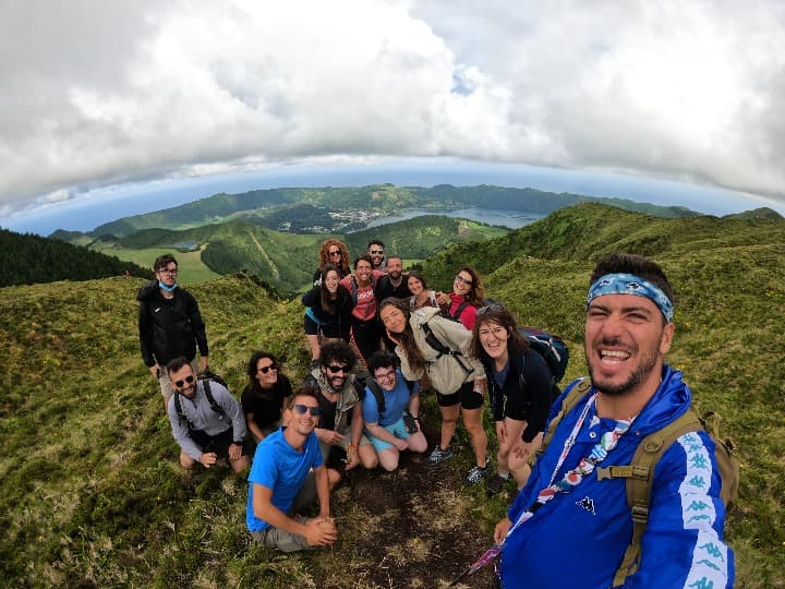 selfie de viajeros weroad en medio de una montaña verde de madeira, al fondo mar y nubes