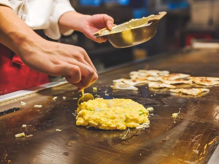 manos de persona cocinando Okonomiyaki en una plancha - weroad