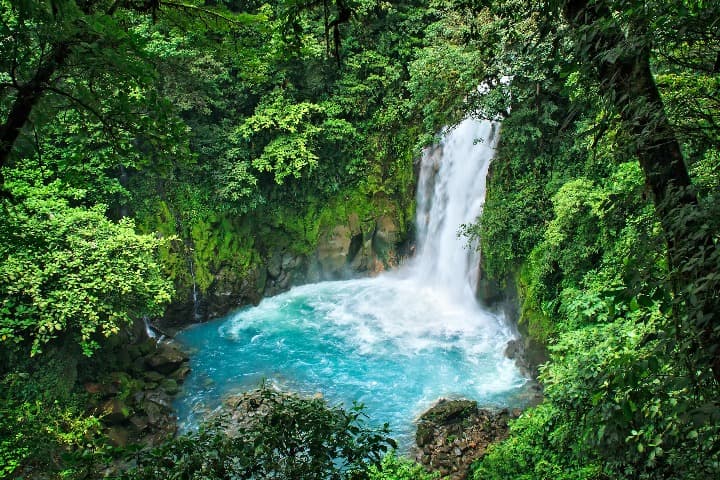 agua que cae desde una cascada a un lago en medio de vegetación verde, volcán tenorio en costa rica
