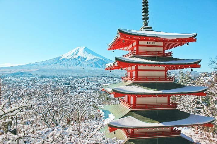 típico edificio japonés rojo en medio de arboles con nieve en invierno, al fondo una montaña - weroad