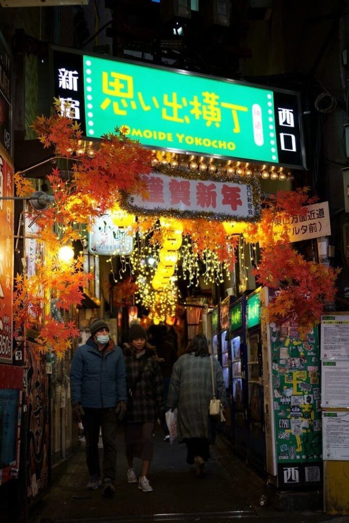 personas caminando en Omoide Yokocho, luces y hojas de arboles a decorar carteles iluminados de noche - weroad