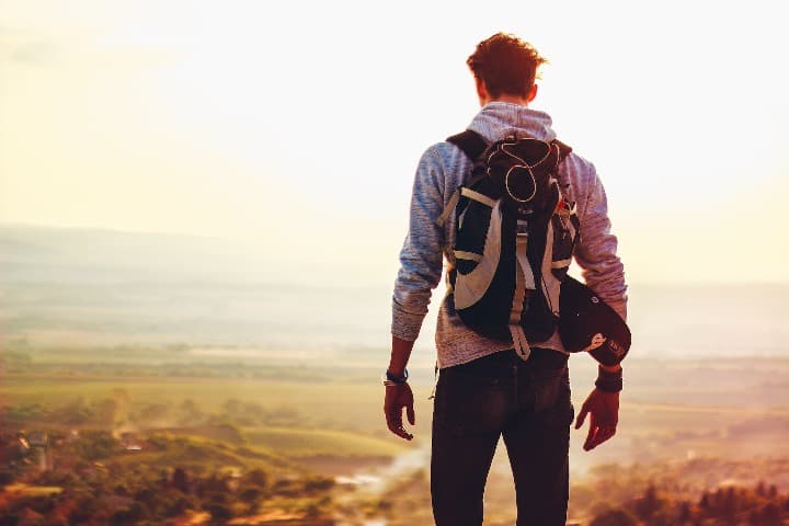 chico con mochila visto de espaldas mientras mira al horizonte en la cumbre de una montaña