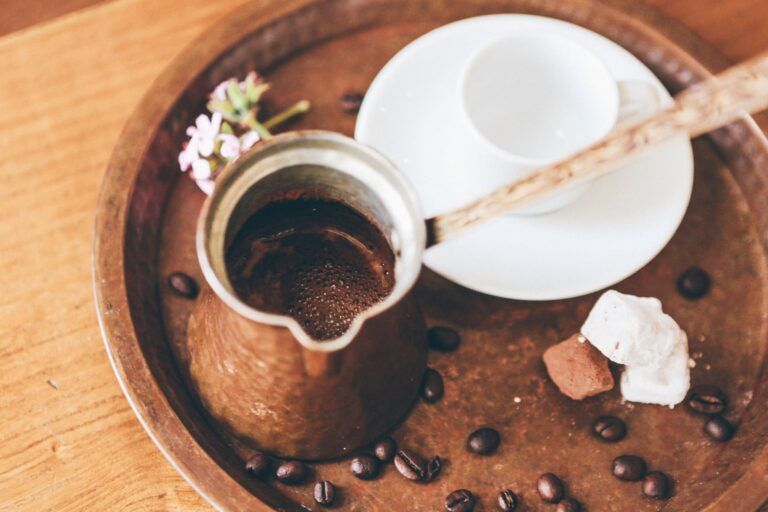 cafetera griega con taza de café al lado, encima de una bandeja con granos de café