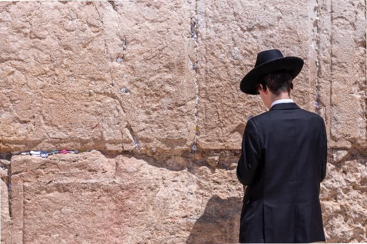 chico judio de espaldas rezando delante del muro de las lamentaciones. jerusalen es buen destino para vivir un inolvidable fin de año en el mundo