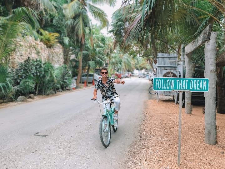chico montado en una bicicleta en una calle en medio de palmeras