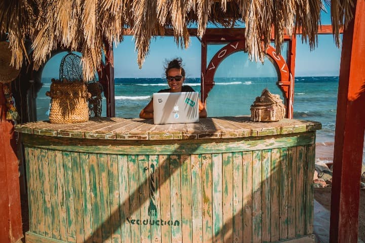 chica delante de un ordenador portatil dentro de un chiringuito en una playa, Mejores destinos para nómadas digitales
