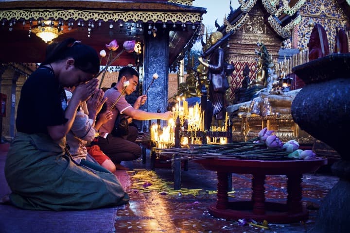 personas rezando con velas y templos detrás en chiang mai, uno de los mejores destinos para nómadas digitales