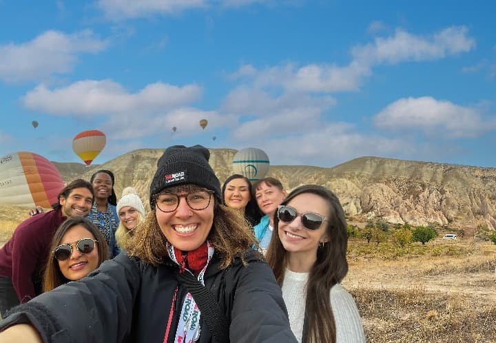 selfie de grupo de viajeros weroad en capadocia, turchia, gllobos aerostáticos detrás