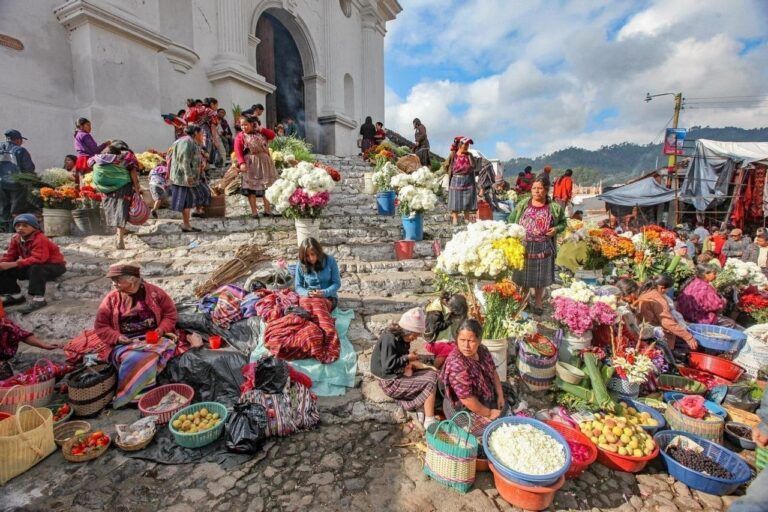 mercado de chichicastenago con mujeres vendiendo productos en cestos de colores, sentadas en las gradas delante de una iglesia