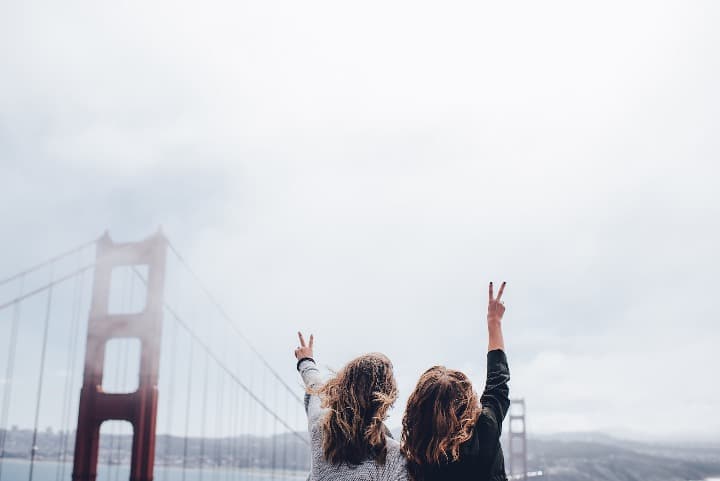 dos chicas de espaldas levantando los brazos y mirando hacia el puente de san francisco