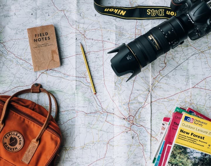 objetos relacionados a un viaje: camara, mochila, mapa, guias de viaje, encima de una mesa