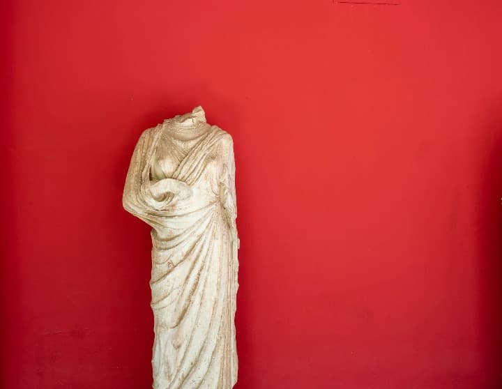 estatua griega delante de pared roja en el museo arqueologico, algo que ver en atenas
