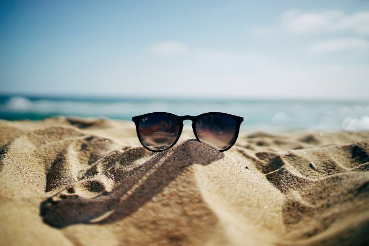 gafas de sol encima de la arena, mar al fondo. viajes verano