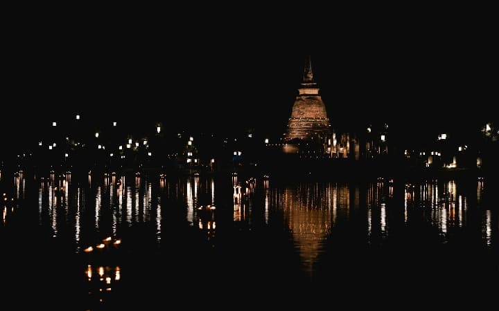 embarcaciones con luces y linternas en una superficie de agua con templo al fondo, de noche, durante el festival de Loy Krathong en Chiang Mai