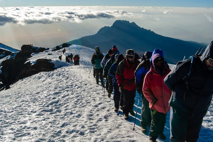 personas subiendo el uhuru peak lleno de nieve