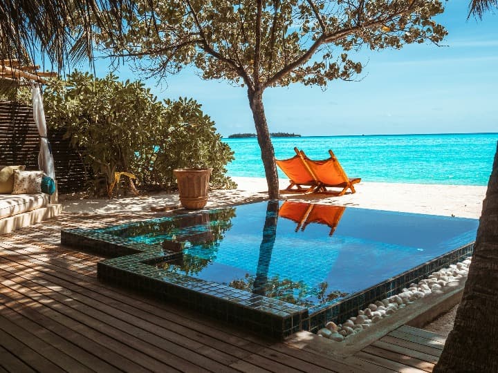 parte exterior de alojamiento en maldivas, tumbonas en la playa, piscina y arbol