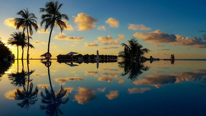 piscina en maldivas con reflejo de cielo y palmas