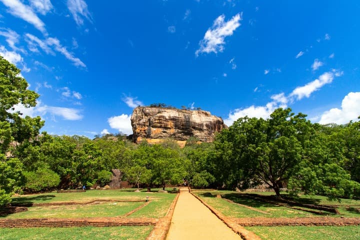 arboles, camino de tierra y al fondo montaña en Sigiriya, Sri Lanka, destino a donde viajar en julio
