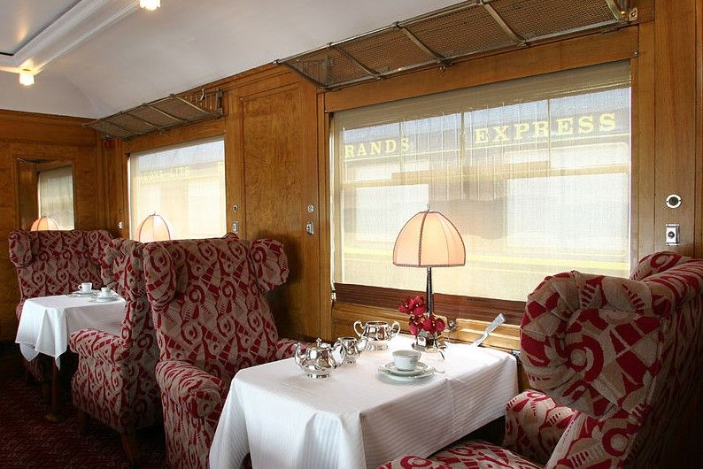 interior elegante del orient express, uno de los mejores viajes en tren que se puedan hacer. butacas y mesa con set de te y lampara