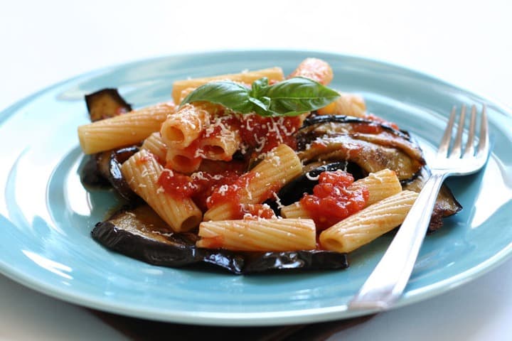 pasta alla norma en un plato turquesa con tenedor, comida tipica de sicilia