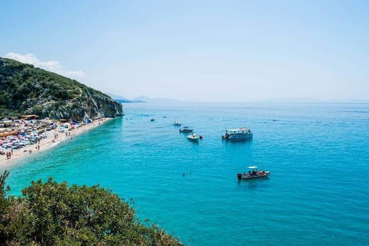 gjipe, barcos y costa llena de sombrillas, montaña verde al final de la cala, una de la playas de albania más bonitas