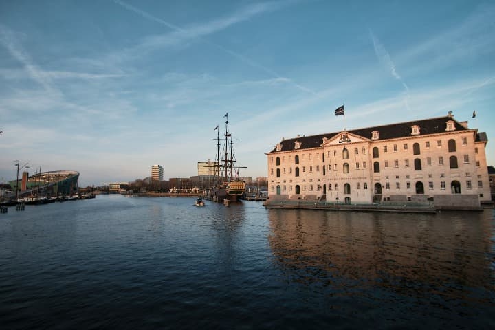 edificio del museo marítimo nacional o Scheepvaartmuseum en medio del agua, un barco delante, algo que ver en amsterdam