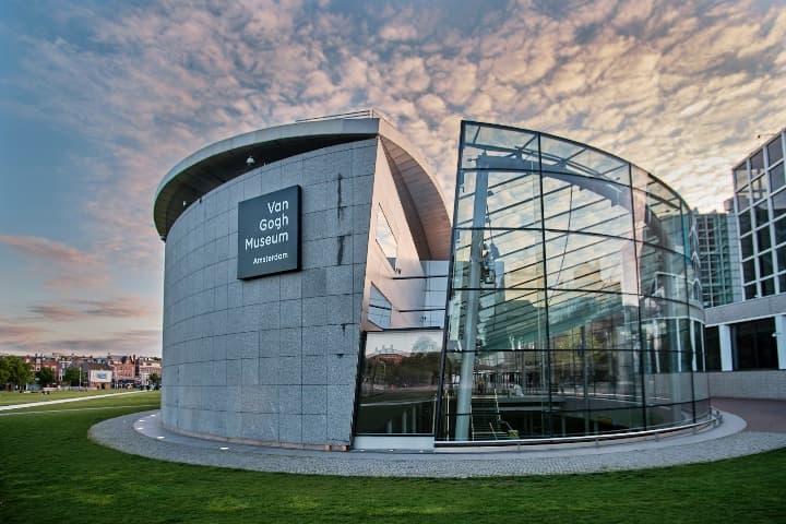 edifcio cilindrico del van gogh museum, cristales y bloques de hormigon, detrás cielo con nubes y cesped