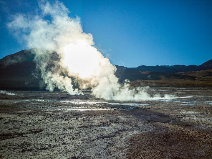 géisere en el tatio, vapor saliendo de la tierra, cielo azul detrás