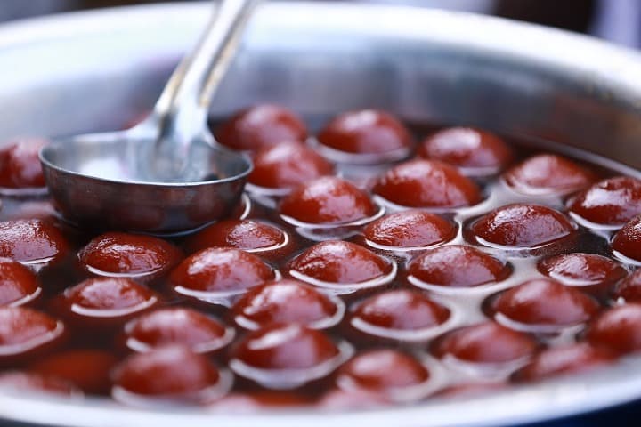 bolitas de Gulab Jamun en un liquido con un cucharón encima, comida típica india