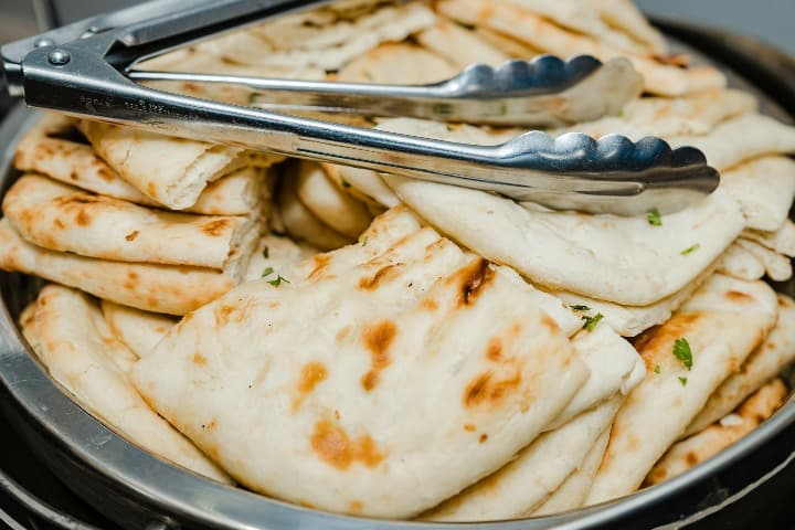 pan naan encima de un plato de acero con pinzas encima, algo que comer en la india