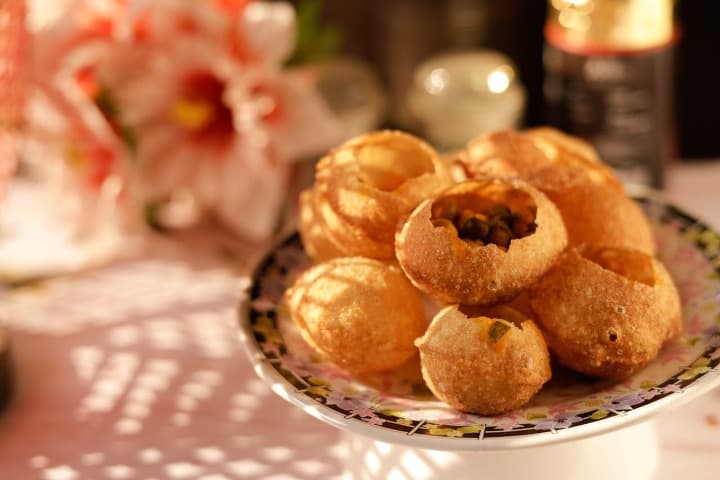 bolitas de panipuri en las que se ve el relleno, estan encima de un plato y detrás hay flores de decoración