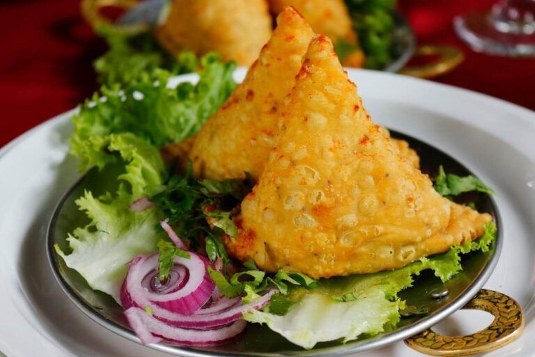 dos samosa en un plato de metal con lechuga y cebolla, comida típica india