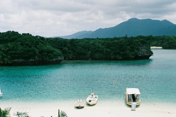 mar verde, bosque y montaá al fondo, barcos en primera línea de playa en kabira bay, en la isla de Ishigaki, algo que ver en okinawa